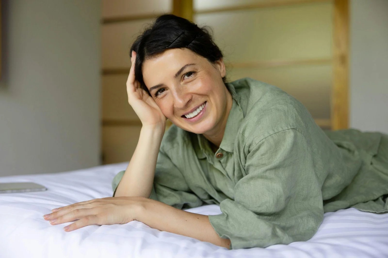 Smiling woman in a green linen shirt resting on a bed