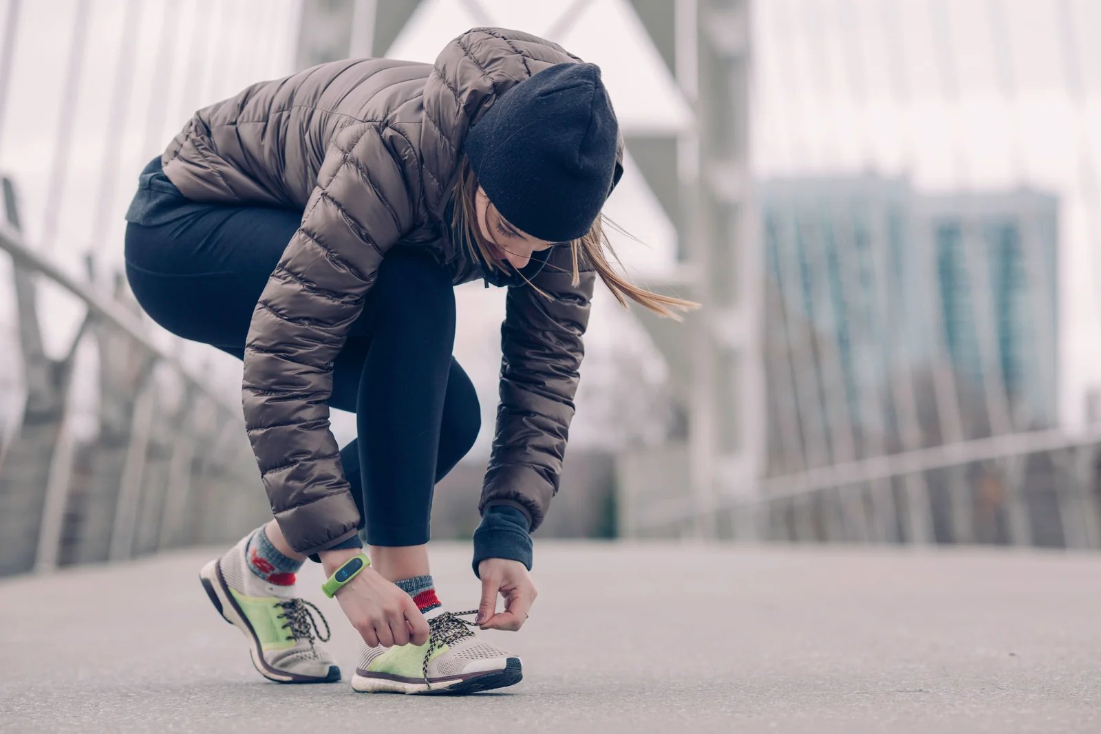 A person in a hooded jacket tying a running shoe before exercising