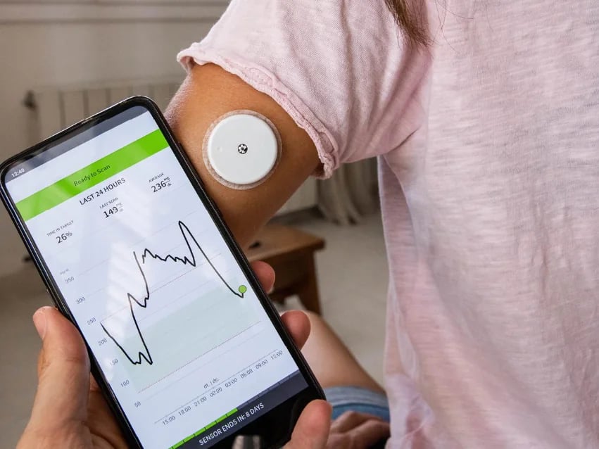 Continuous glucose monitor sensor and a phone showing a glucose graph